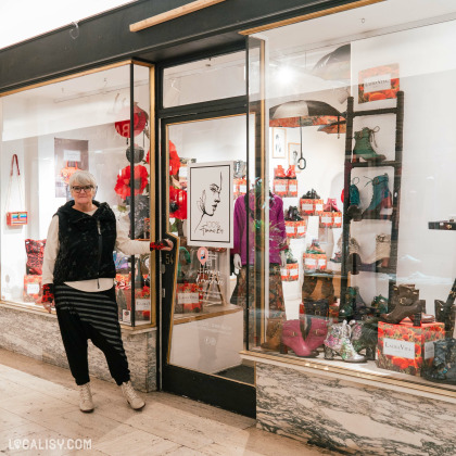 Devanture du magasin “100% femme.bis” à Liège. La façade en verre expose divers articles, notamment des sacs et peut-être des vêtements. Une personne, dont le visage est masqué, se tient à l’entrée, tenant la porte ouverte.