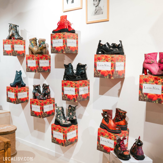 L’intérieur du magasin “100% femme.bis” à Liège. On y voit divers styles de chaussures pour femmes, chacune placée sur des boîtes rouges avec la marque “Laura Vita” imprimée dessus.