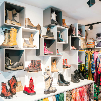 L’intérieur de la boutique “LELLOU” à Liège, avec une étagère murale remplie de divers styles de chaussures. La collection comprend des bottes de différentes couleurs et motifs, allant des classiques marron et noir aux rouges et roses vibrants.