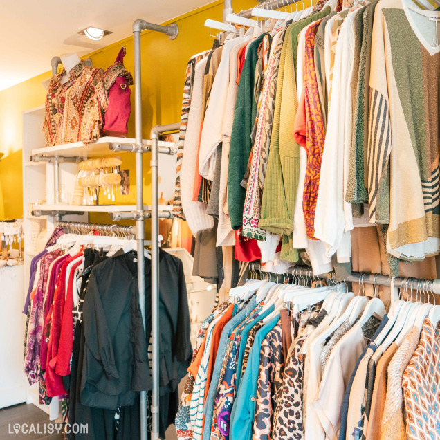 Une variété de vêtements colorés suspendus à des portants, avec différents motifs et textures chez "Nao" à Liège.