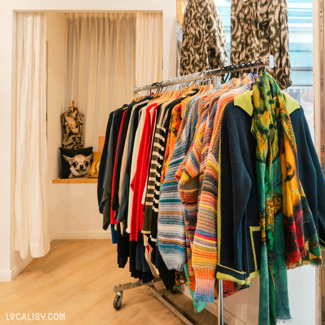 Des portants de vêtements colorés, principalement des pulls avec divers motifs, et un élément décoratif ressemblant à un panda en arrière-plan à  l’intérieur du magasin “Miss Bambou” à Liège.