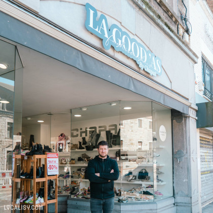 Devanture du magasin “Chapati/La Good’as” à Aywaille, une vitrine avec divers articles, notamment des chaussures, et une pancarte indiquant une vente avec “TOUT À -50%”.