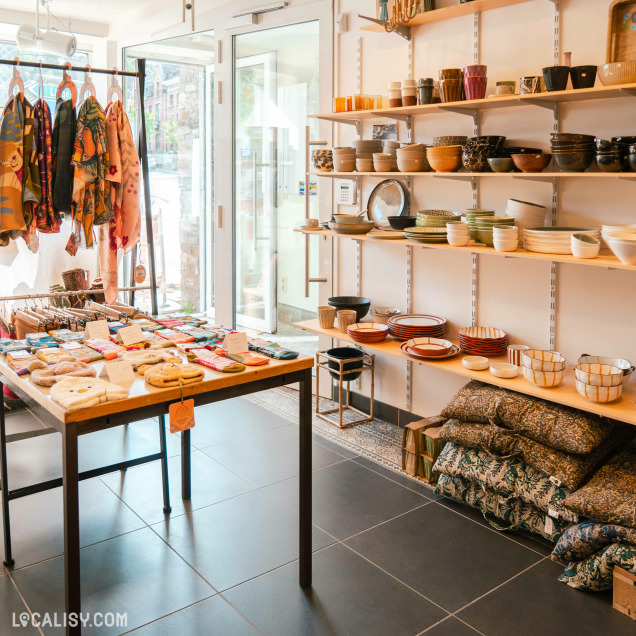 L’intérieur du magasin “Orangeola by Math” à Tilff, avec des étagères bien organisées exposant divers articles de poterie colorée, textiles et objets de décoration.