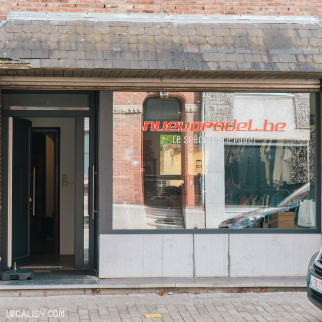 Devanture du magasin “NuevoPadel” à Tilff, avec une porte en verre encadrée de noir et une grande vitrine affichant le site “nuevopadel.be” et le slogan “Le Spécialiste Padel”.