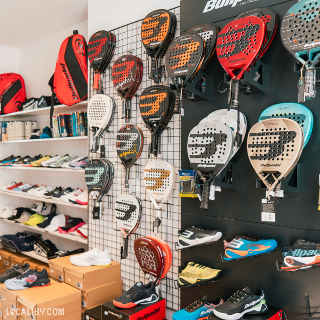 L’intérieur du magasin “NuevoPadel” à Tilff, avec un mur exposant divers raquettes de padel et des chaussures de sport sur des étagères en dessous.