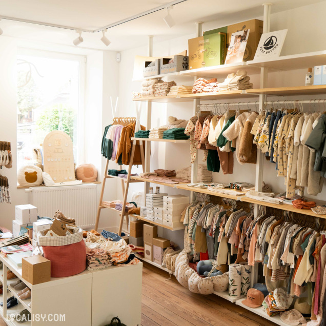 L’intérieur du magasin “Culottes Courtes” à Heusy, avec des vêtements pour enfants soigneusement disposés sur des étagères et des cintres. Le magasin est bien éclairé par la lumière naturelle et présente une ambiance accueillante et organisée.