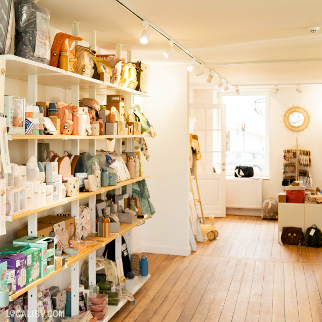 L’intérieur du magasin “Culottes Courtes” à Heusy, avec des étagères bien organisées exposant divers articles pour enfants, comme des jouets, des sacs et d’autres accessoires. Le magasin est bien éclairé et présente une ambiance chaleureuse et accueillante.