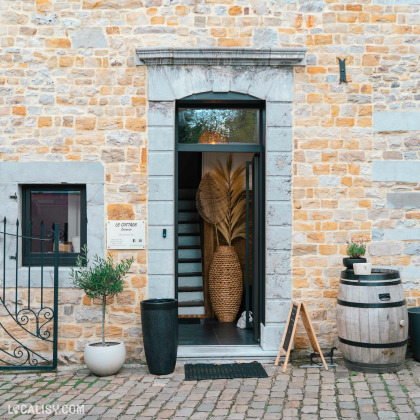 Devanture du magasin “Le Cottage Interior” à Charneux, avec une façade en pierre, une porte noire vitrée, et des plantes décoratives à l’extérieur.