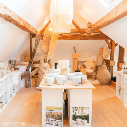 L’intérieur du magasin “Le Cottage Interior” à Charneux, avec une décoration rustique et chaleureuse, des poutres apparentes, des meubles blancs, et divers articles de décoration.