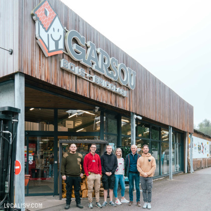 Devanture du magasin “Garsou Bois & Bricolage” à Theux. La façade moderne est en bois avec de grandes lettres indiquant le nom du magasin. Devant le magasin, sept personnes sont alignées, faisant face à la caméra.