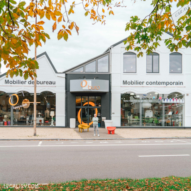 Devanture du magasin “Oburo” à Liège avec de grandes fenêtres en verre affichant divers meubles, un logo orange distinctif au-dessus de l’entrée. Le bâtiment a un design moderne avec des couleurs grises et blanches.