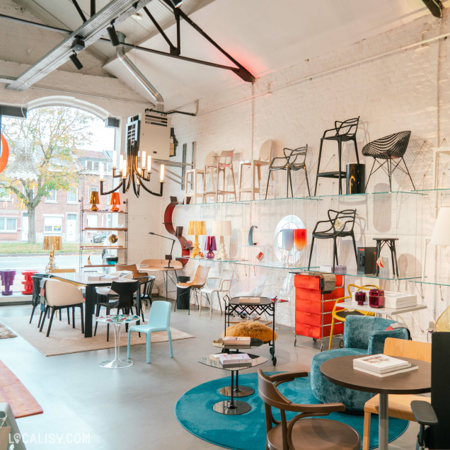 Divers meubles exposés, notamment des chaises, des tables et des étagères au magasin “Oburo” à Liège. L’espace a des murs blancs et un plafond haut avec des poutres et des conduits apparents.