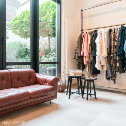 L’intérieur du magasin “Lulu Store” à Liège, avec une sélection de vêtements suspendus sur un portant, un canapé en cuir marron et une petite table avec des livres.