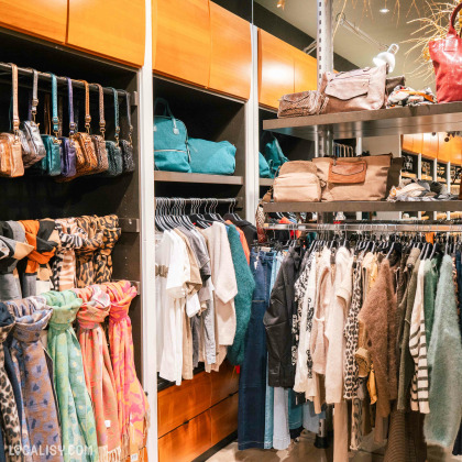 L’intérieur de la boutique “Coco Bijoux et Accessoires” à Liège, avec divers vêtements et accessoires exposés sur des étagères et des portants.