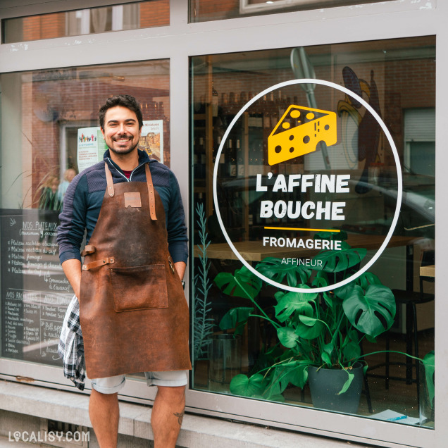 Devanture de la fromagerie “L’affine Bouche” à Liège, avec une personne en tablier debout devant la vitrine.