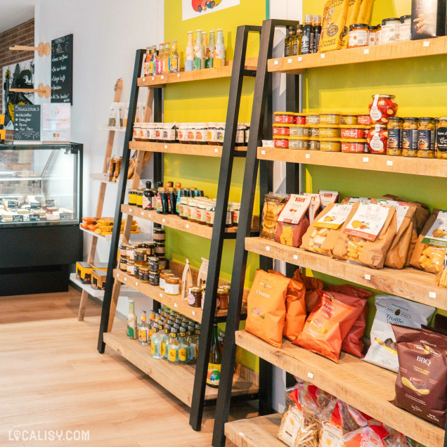 L’intérieur de la fromagerie “L’affine Bouche” à Liège, avec des étagères en bois remplies de divers produits alimentaires emballés, y compris des bouteilles, des bocaux et des boîtes.