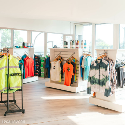 L’intérieur du magasin "Respire Sports" à Jalhay, avec des portants et des présentoirs affichant divers vêtements de sport, y compris des chemises, des vestes et d’autres tenues de sport colorées.