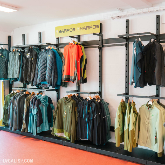 L’intérieur du magasin "Respire Sports" à Jalhay, avec un présentoir mural de vestes de différentes couleurs et styles. Au-dessus du présentoir, il y a une enseigne avec le texte “YARPOS YARPOS” en lettres jaunes.