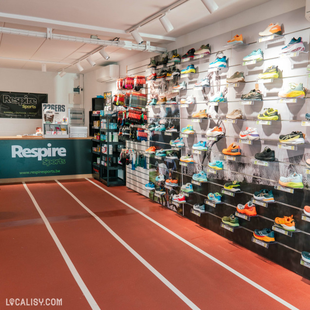 L’intérieur du magasin “Respire Sports” à Jalhay, avec une variété de chaussures de sport exposées sur des étagères murales. Le sol est conçu pour ressembler à une piste d’athlétisme.