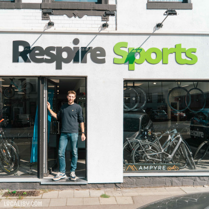 Devanture du magasin “Respire Sports Bike” à Spa. Le nom du magasin est affiché en grandes lettres vertes au-dessus de l’entrée. Une personne se tient à la porte ouverte, et la vitrine expose divers vélos.