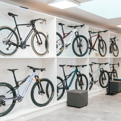 L’intérieur du magasin “Respire Sports Bike” à Spa, avec plusieurs vélos exposés sur des supports blancs contre un mur blanc. Le sol est de couleur claire et il y a un cube de siège au centre.