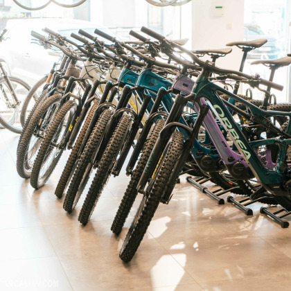 Une rangée de vélos de montagne soigneusement exposés. Les vélos sont alignés avec leurs roues avant face à la caméra à l’intérieur du magasin “Respire Sports Bike” à Spa.