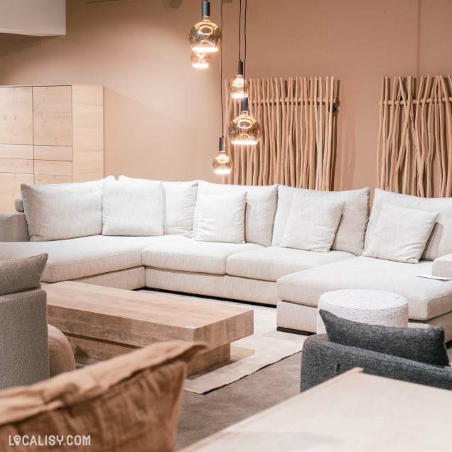 Un grand canapé d’angle clair autour d’une table centrale en bois chez  “Petit Bairro” à Saint-Georges-sur-Meuse. Des luminaires suspendus avec des ampoules à filament exposé ajoutent une touche moderne.