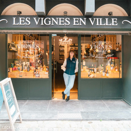 Devanture du magasin “Les Vignes en Ville” à Liège. La façade est noire avec le nom du magasin écrit en blanc, encadré par deux grandes vitrines présentant diverses bouteilles. Un tableau noir est placé devant une des vitrines.