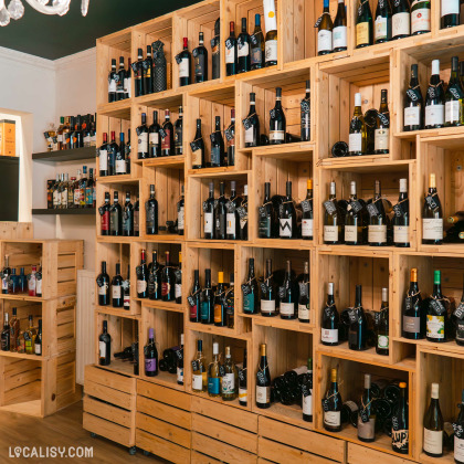 L’intérieur du magasin “Les Vignes en Ville” à Liège, avec des étagères en bois remplies de diverses bouteilles de vin.