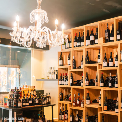 L’intérieur du magasin “Les Vignes en Ville” à Liège, avec une grande étagère en bois remplie de diverses bouteilles de vin.