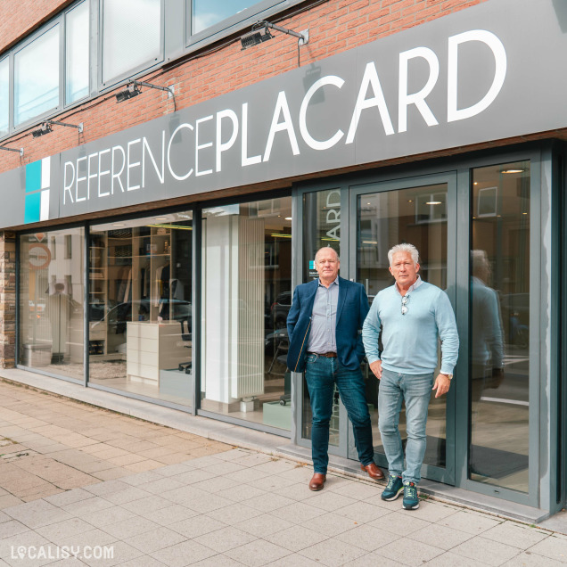 Devanture du magasin “ReferencePlacard” à Grivegnée. La façade est moderne avec de grandes fenêtres et une palette de couleurs grises. Deux personnes se tiennent devant le magasin, leurs visages étant floutés pour préserver leur vie privée.