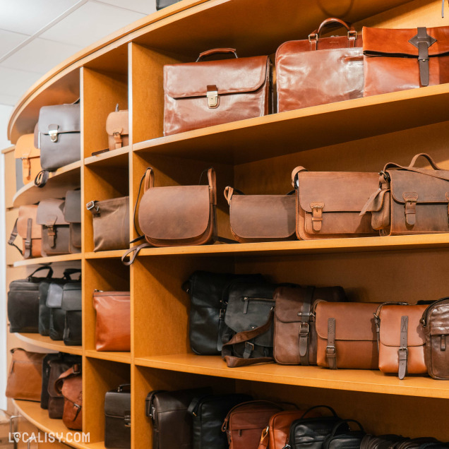 Une variété de sacs en cuir exposés sur des étagères en bois à la "Maroquinerie Marie" à Liège. Les sacs sont de différentes tailles et nuances de marron et de noir.