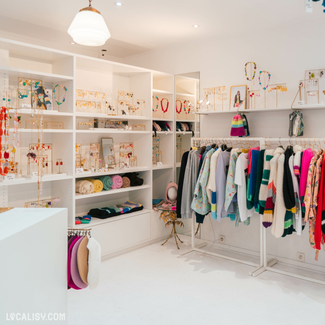 L’intérieur de la boutique "Ariane Lespire" à Liège. Les murs et le sol sont blancs, avec des étagères exposant divers accessoires comme des colliers et des bracelets.