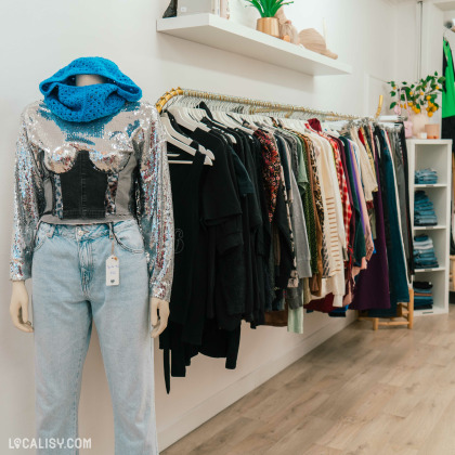 L’intérieur de la boutique "Holà Stasia" à Jemeppe. Un mannequin porte un jean bleu clair et un haut noir avec des paillettes argentées, accessoirisé d’une écharpe bleue.