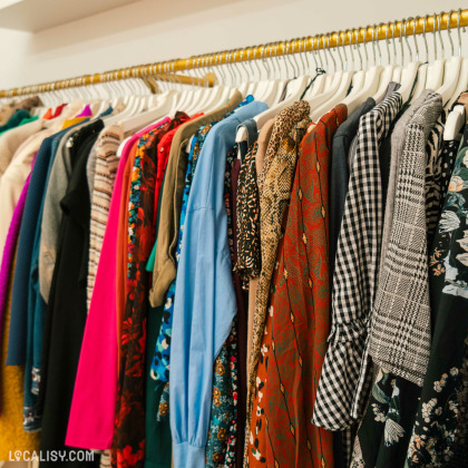 Variété de vêtements suspendus sur un portant dans le magasin "Holà Stasia" à Jemeppe. Les vêtements présentent une gamme de couleurs et de motifs, suggérant une sélection diversifiée.