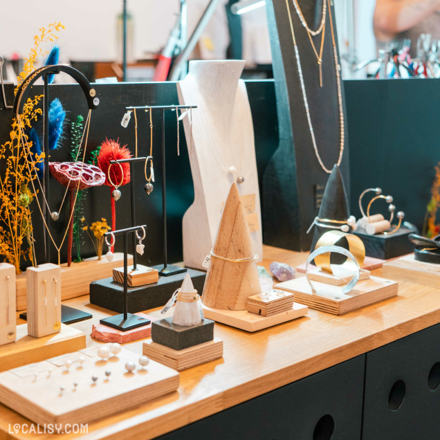 Un présentoir de bijoux à l’intérieur du magasin "Lara Malherbe" à Liège. La collection comprend des colliers, des bracelets et des bagues, présentés sur différents types de supports pour mettre en valeur chaque pièce.