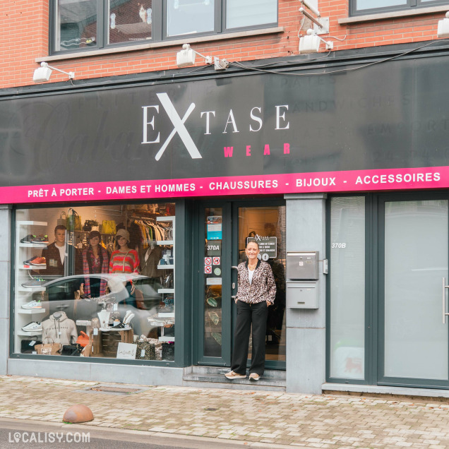 La devanture du magasin "Extase wear" à Flémalle, avec une enseigne noire et blanche et une vitrine exposant des vêtements.