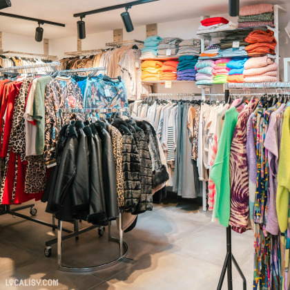 L’intérieur du magasin "Extase wear" à Flémalle, avec divers vêtements colorés exposés sur des portants et des étagères.