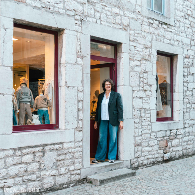 Devanture du magasin “Pierre et le Loup” à Aywaille. La devanture en pierre comporte deux grandes vitrines avec des mannequins habillés en vêtements pour enfants. Une personne se tient à l’entrée, mais son visage est flouté pour des raisons de confidentialité.