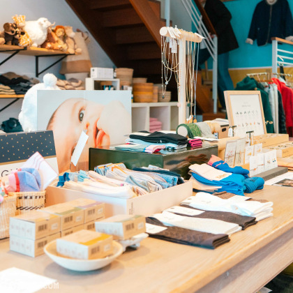 L’intérieur de la boutique “Pierre et le Loup” à Aywaille. Le magasin est bien organisé, avec des vêtements, des accessoires et des objets décoratifs exposés sur des tables en bois et des étagères.