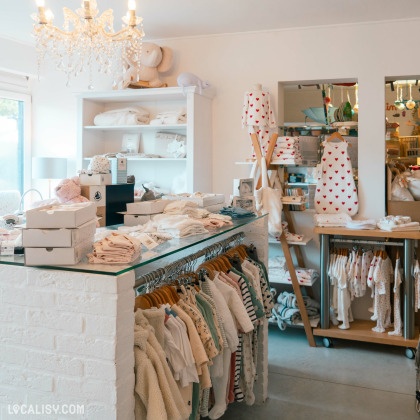 Des vêtements et des accessoires pour enfants exposés sur des portants et des étagères. Un comptoir en briques peintes en blanc est visible à l’intérieur du magasin “Basile et Lola” à Angleur.