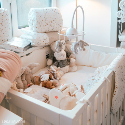 Un coin douillet du magasin “Basile et Lola” à Angleur, avec un berceau rempli de peluches et entouré de textiles et de coussins aux tons doux, créant une atmosphère chaleureuse et accueillante pour les clients.