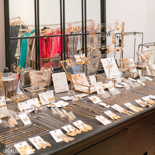 Un présentoir de bijoux dans le magasin “By Four Seasons” à Chênée. On y voit des colliers, des boucles d’oreilles et des bracelets, certains en tons dorés et d’autres ornés de pierres ou de perles.