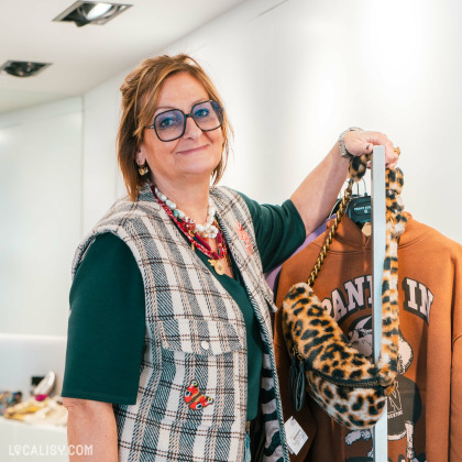 Intérieur du magasin '' Icone'' avec MARIE-LUCE tenant un sac à motif léopard et un sweat-shirt marron, souriant dans un environnement de boutique moderne.