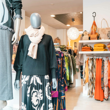 Intérieur moderne du magasin ''Marie-Lisa'' à Spa présentant des vêtements, foulards, écharpes, sacs.