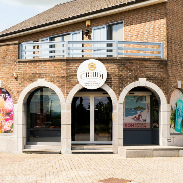 Devanture du magasin de spiritueux C’Rhum à Battice, avec une façade en briques présentant trois fenêtres en arc et une porte d’entrée centrale. Au-dessus de la porte, une enseigne affiche le nom du magasin “C’Rhum” et son logo.