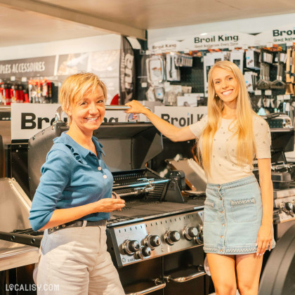 L’intérieur d’un magasin de mobilier de jardin Fortemps SRL à Soumagne, avec deux personnes présentes au premier plan. Le magasin est bien approvisionné avec divers articles liés à la cuisine en plein air et à l’entretien du jardin visibles sur les étagères.