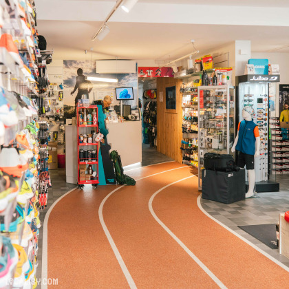 L’intérieur du magasin d'articles de course à pied Xrun à Battice, avec une variété d’équipements et de vêtements de sport exposés sur des étagères murales et des présentoirs centraux. Un aspect notable est le sol, qui ressemble à une piste de course, ajoutant une touche thématique au design du magasin.