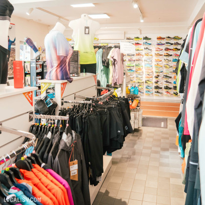 L’intérieur du magasin d'articles de course à pied Xrun à Battice, avec divers vêtements et chaussures de sport exposés. Le magasin est bien éclairé et organisé, répondant aux besoins des athlètes.