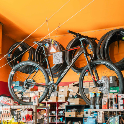 L’intérieur du magasin de vélos Total Bike à Liège, avec une variété de vélos et de produits liés au cyclisme. Un vélo est mis en avant avec une étiquette de prix de 650 euros. Le magasin est bien approvisionné avec des articles tels que des pneus de vélo, des boîtes contenant probablement des accessoires ou des pièces de vélo.